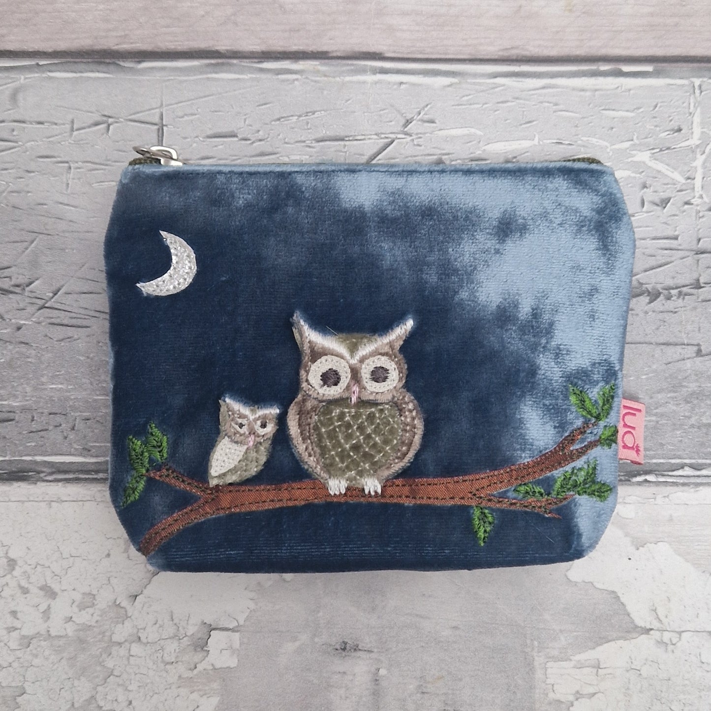 Blue pouch with embroidered owls and a branch on a textured gray background