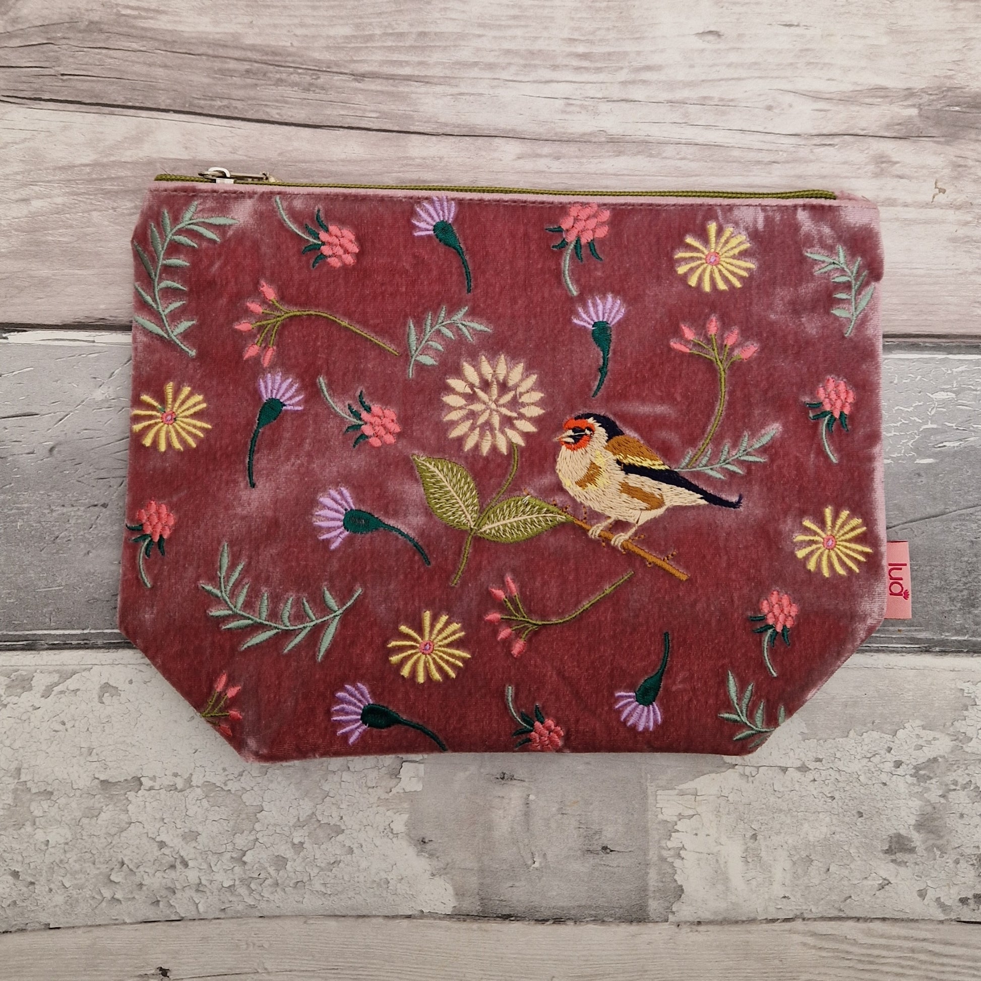 Pink velvet pouch decorated with flowers of pink and purple and embroidered depiction of a Goldfinch.