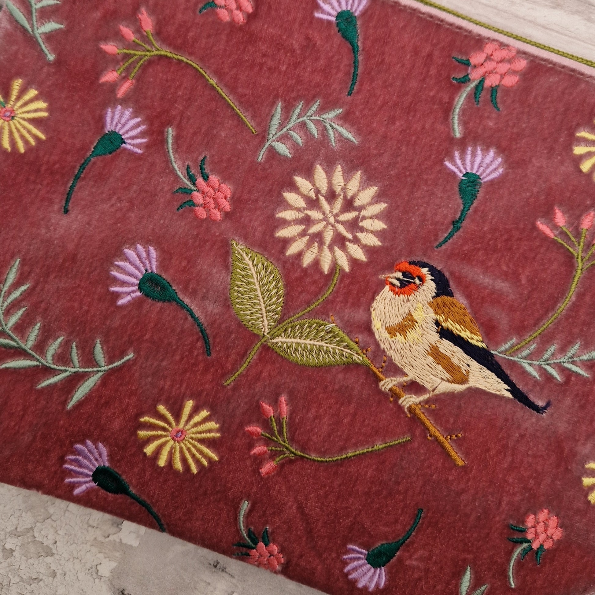 Pink velvet pouch decorated with flowers of pink and purple and embroidered depiction of a Goldfinch.