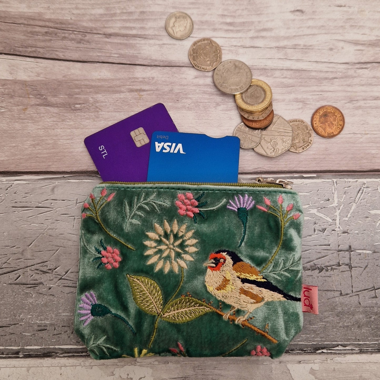 Green velvet coin purse decorated with flowers of pink and purple and embroidered depiction of a Goldfinch.