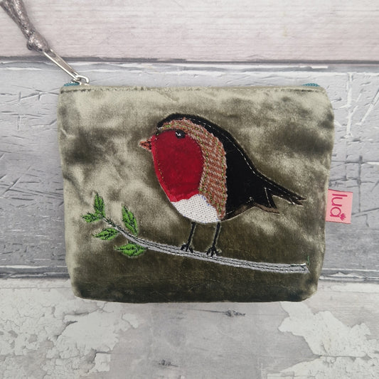 An olive green velvet coin purse featuring an embroidered robin bird on a branch. The coin purse has a silver zipper with a matching strap and a small pink tag on the side.