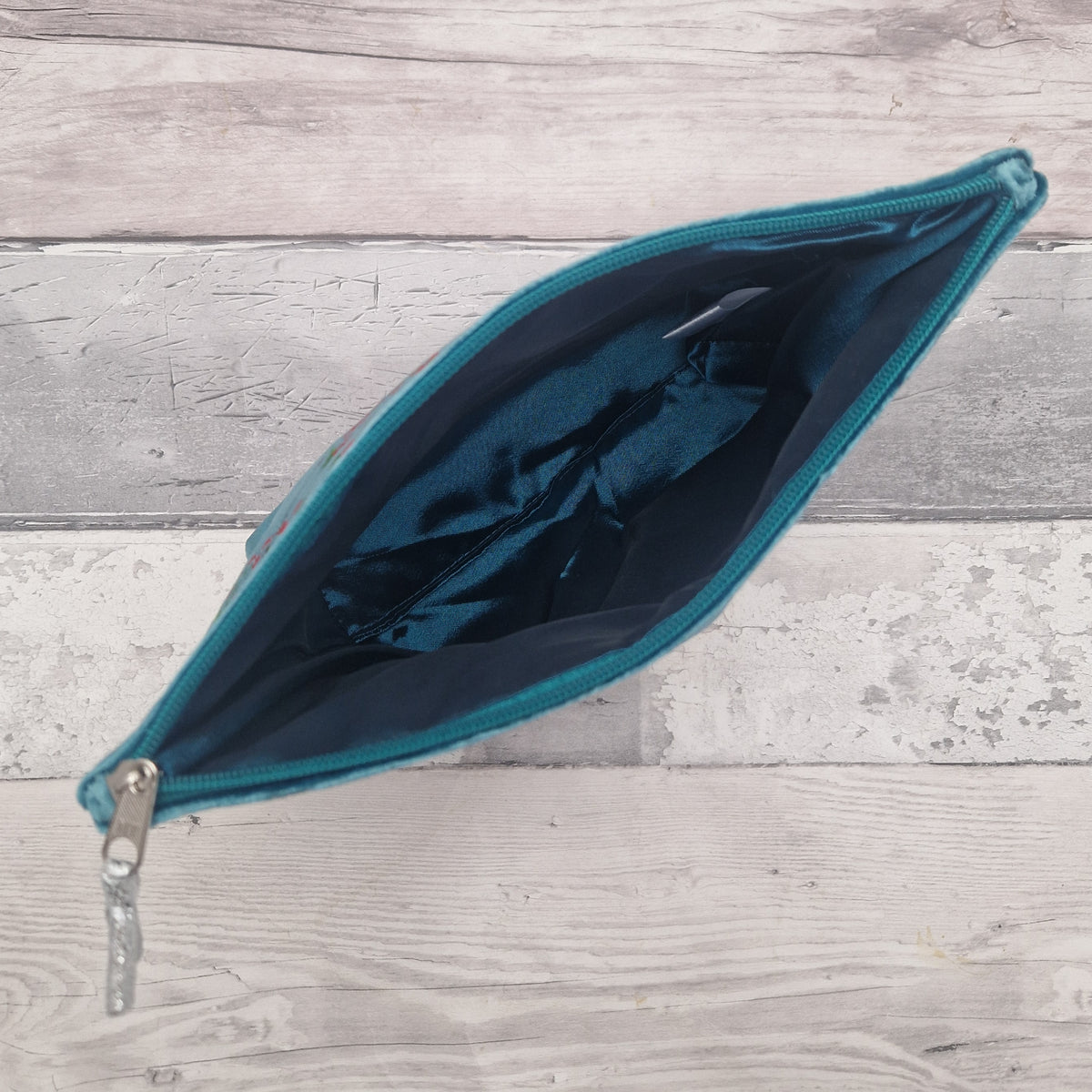 An open teal zippered pouch with a dark blue interior, shown on a light gray wood plank background.