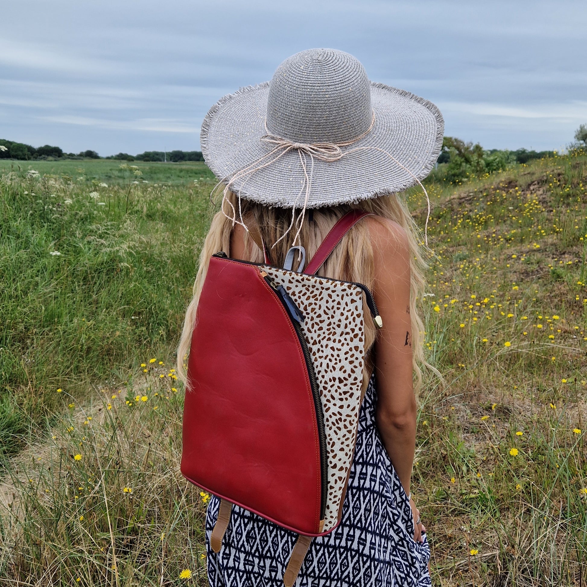 Girl wearing Red leather backback with white cow hide panel decorated in brown spots.