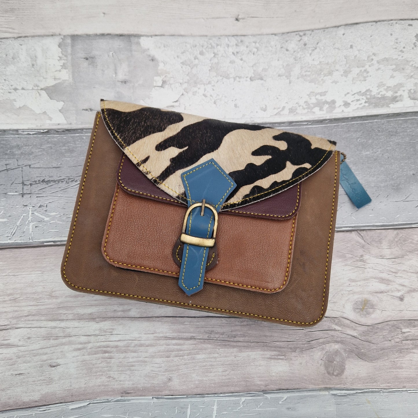 Brown leather satchel style bag with textured front panel in cow hide print.