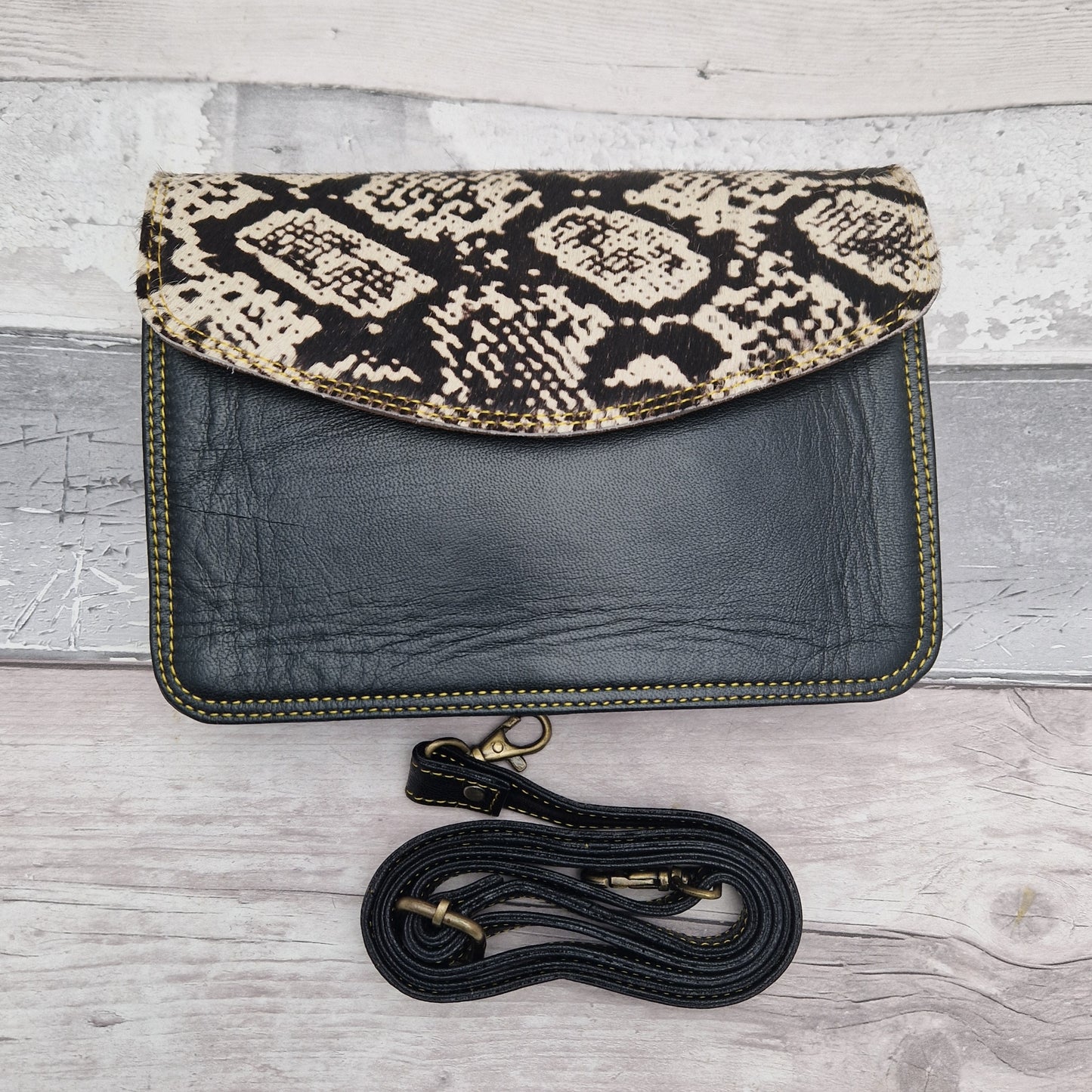 Black leather bag with envelope style and textured panel of snakeskin print.