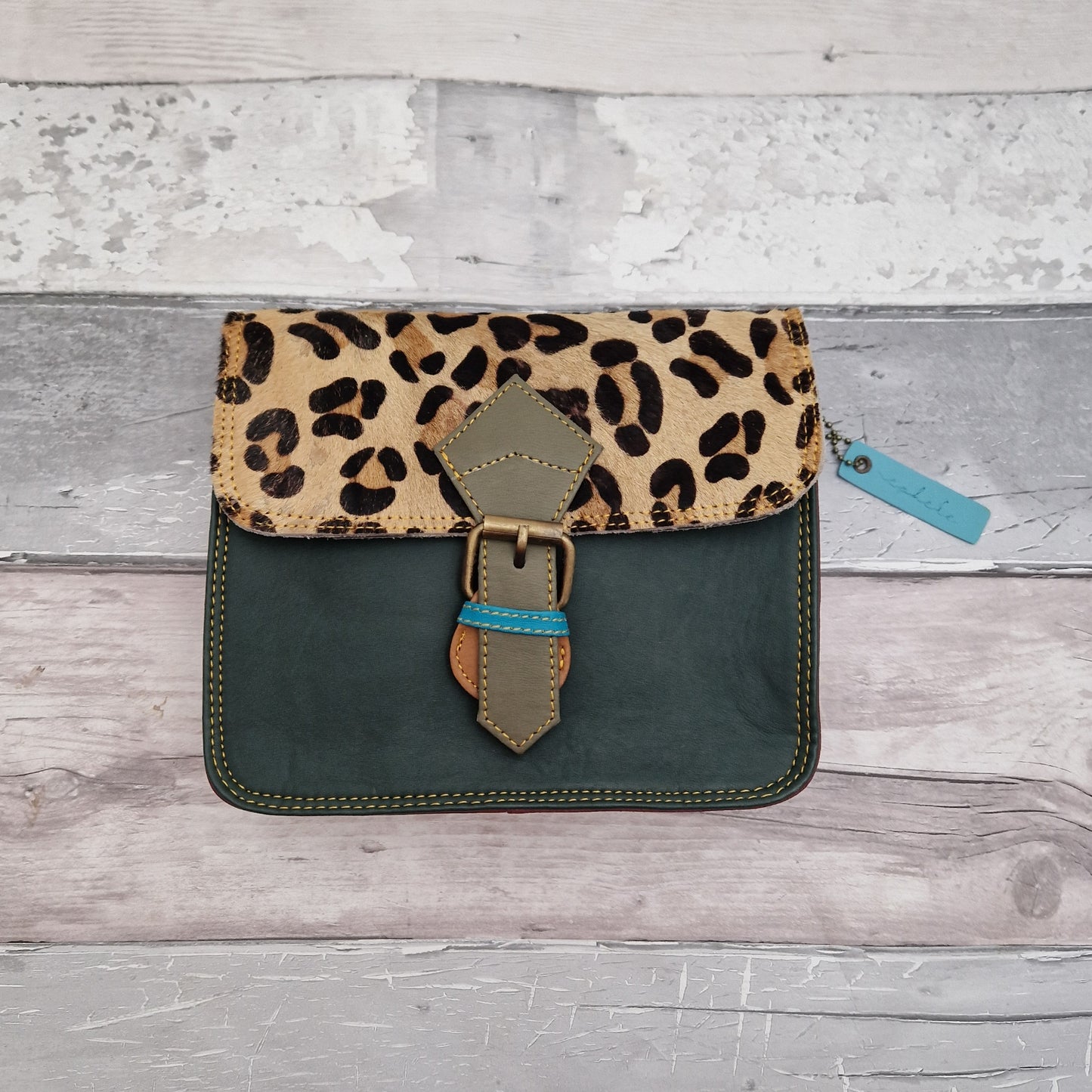 Green leather cross body bag with textured panel of leopard print.