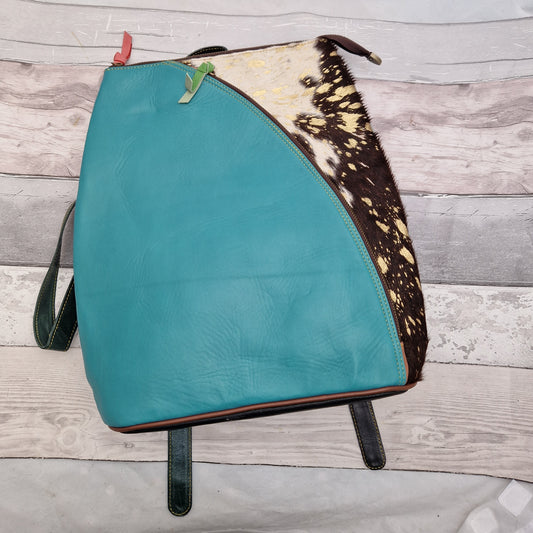 Turquoise blue leather back pack with a textured panel of black and white cow print.