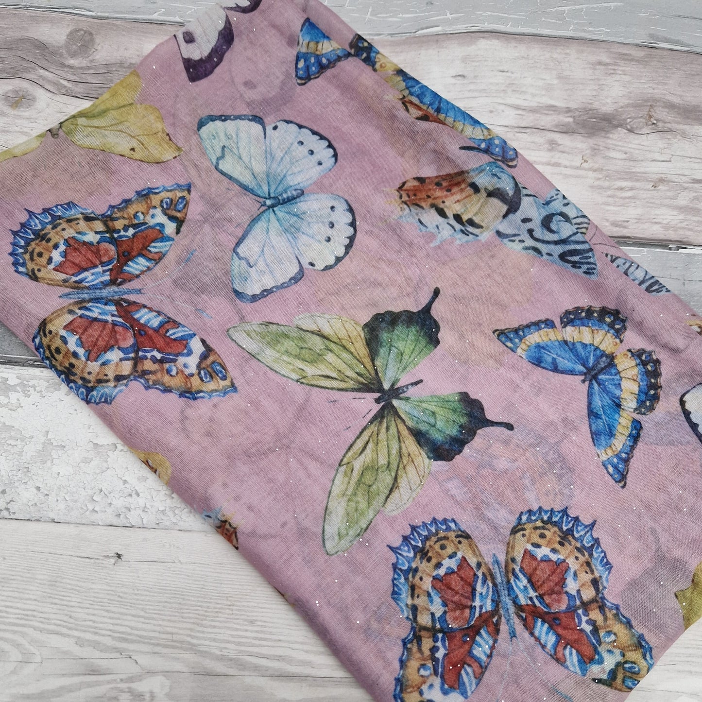 Dusky pink scarf decorated with a collection of vividly coloured butterflies and finished with silver sparkles.