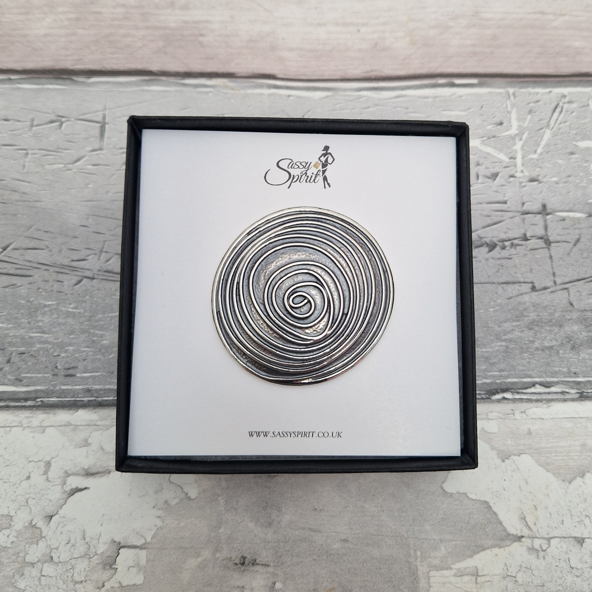 Decorative metal spiral on a white card with 'Sassy Spirit' branding, framed against a textured gray background.