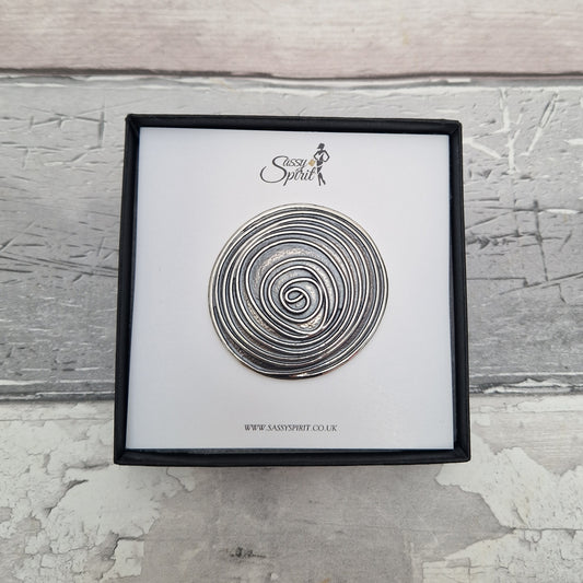 Decorative metal spiral on a white card with 'Sassy Spirit' branding, framed against a textured gray background.