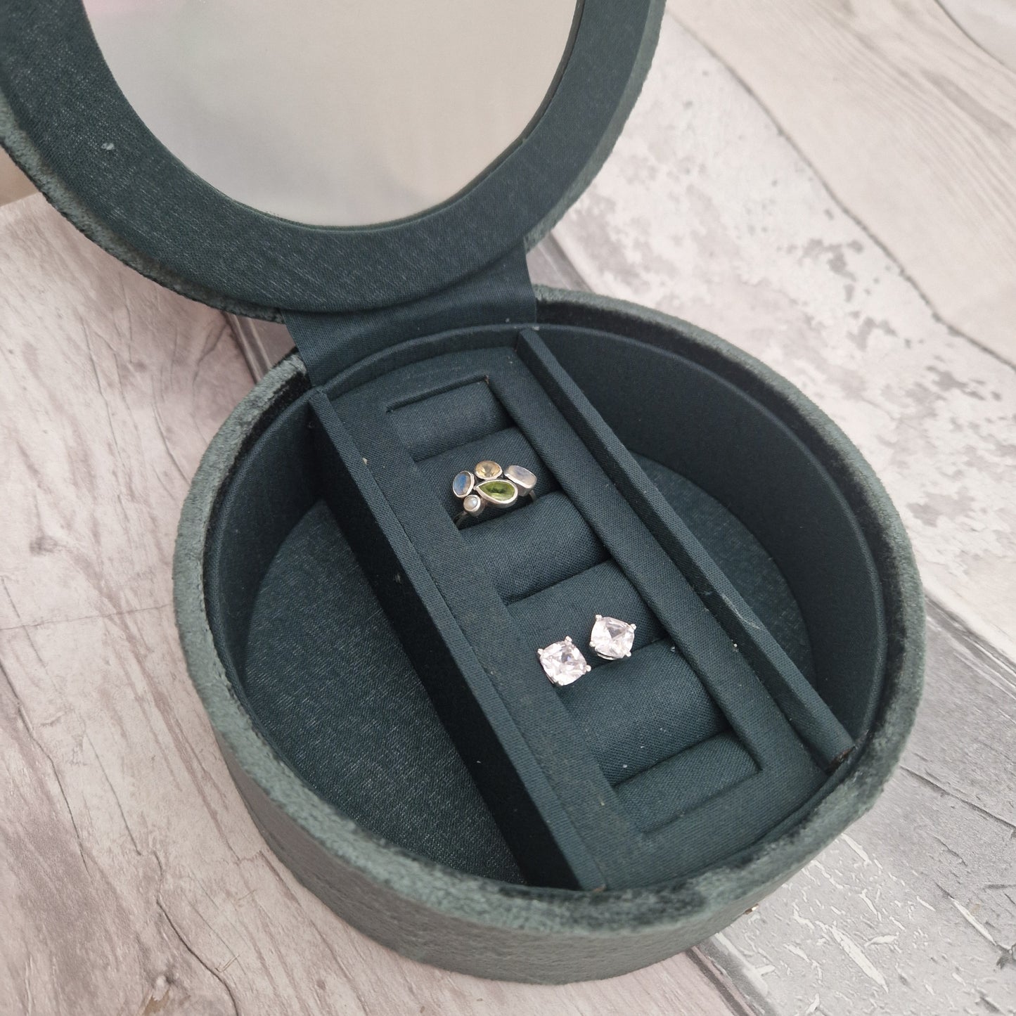 Round green jewelry box with two pairs of earrings inside on a wooden surface