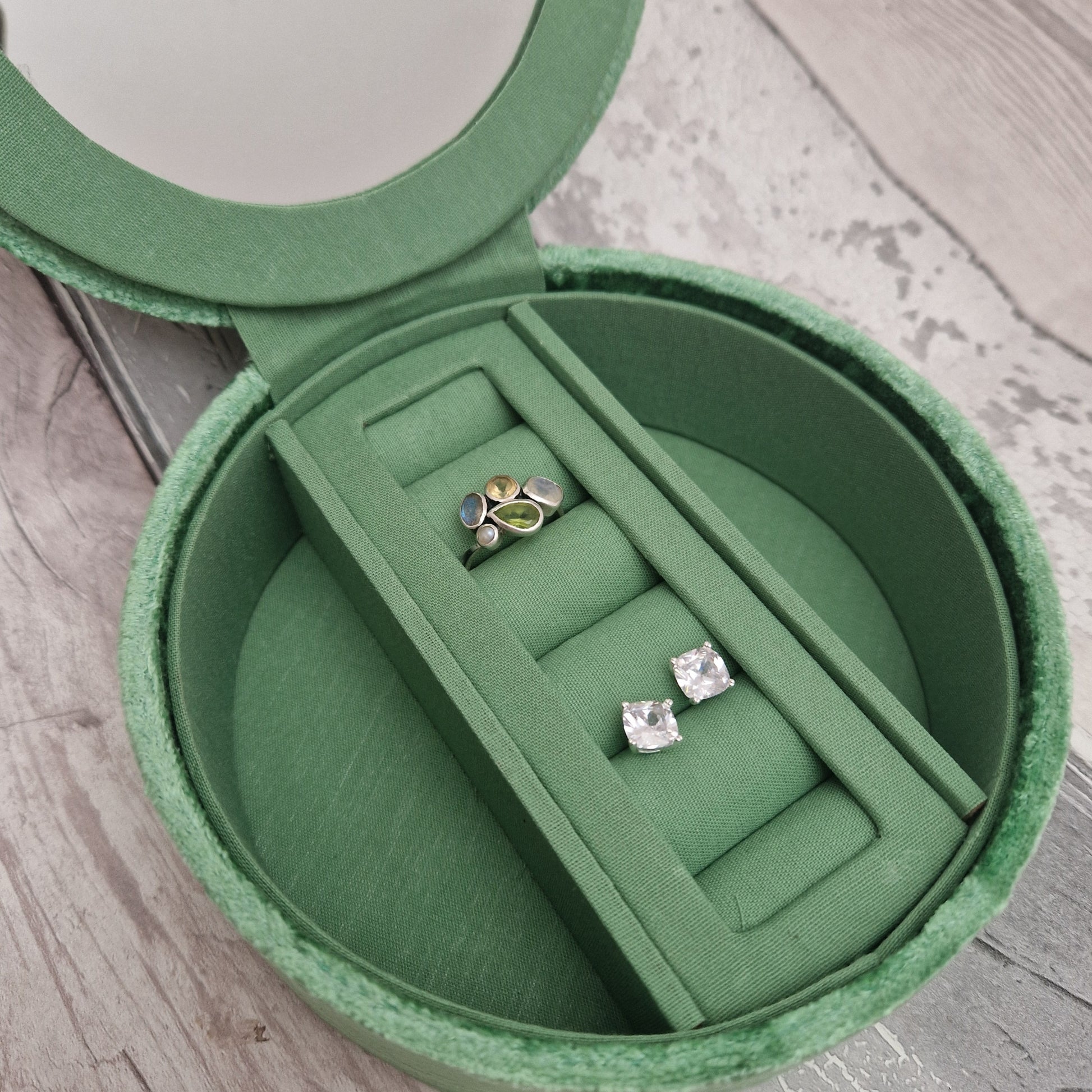 Green jewelry box with two pairs of earrings inside on a wooden surface