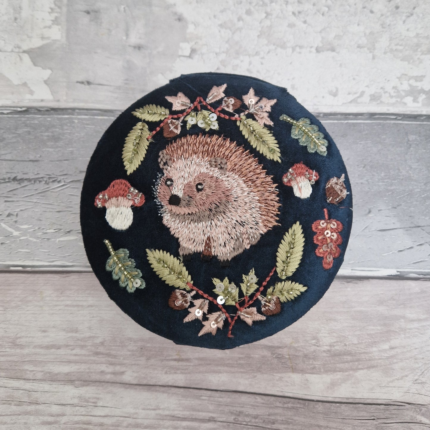 Navy velvet covered jewellery bow with embroidered scene of a Hedgehog amongst woodland leaves and mushrooms. The design is finished with sequins and beads.