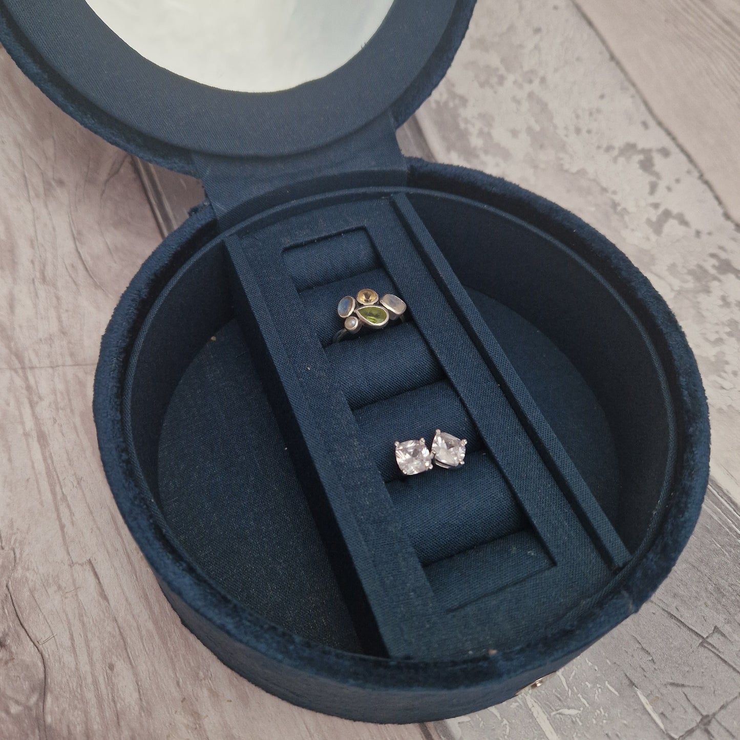 Open navy blue jewelry box with two pairs of earrings inside on a wooden surface.