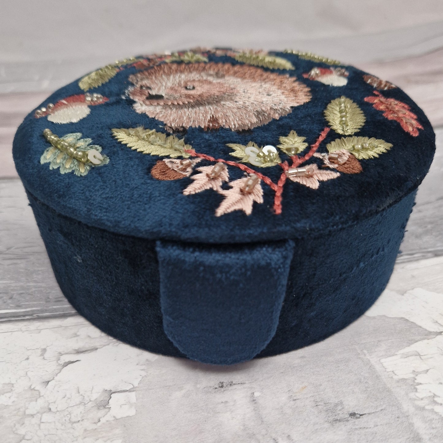 Navy velvet covered jewellery bow with embroidered scene of a Hedgehog amongst woodland leaves and mushrooms. The design is finished with sequins and beads.