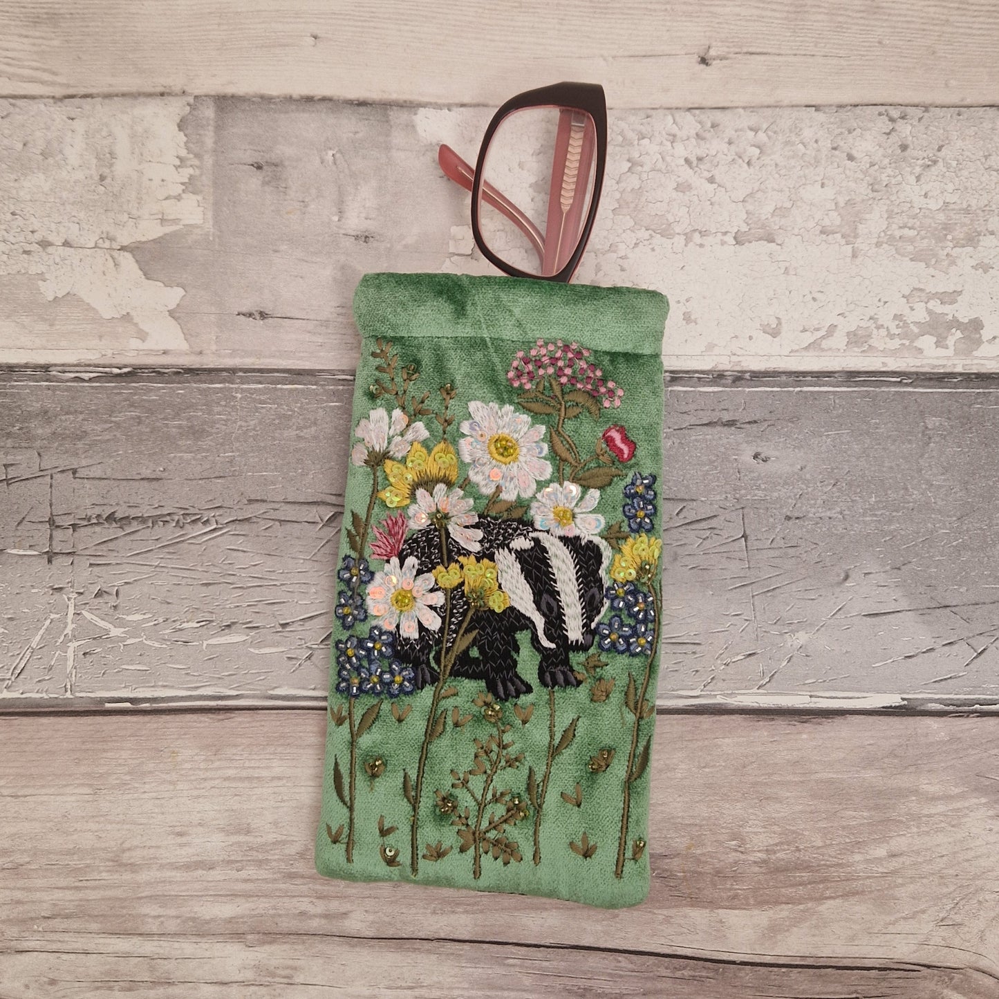 Green velvet glasses case decorated with an embroidered scene featuring a Badger in a flower garden. The scene is finished with beads and sequins.