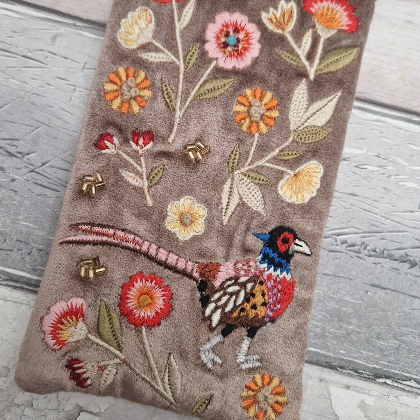 Fawn coloured velvet glasses case decorated with an embroidered scene featuring a Pheasant in a flower garden. The scene is finished with beads and sequins.