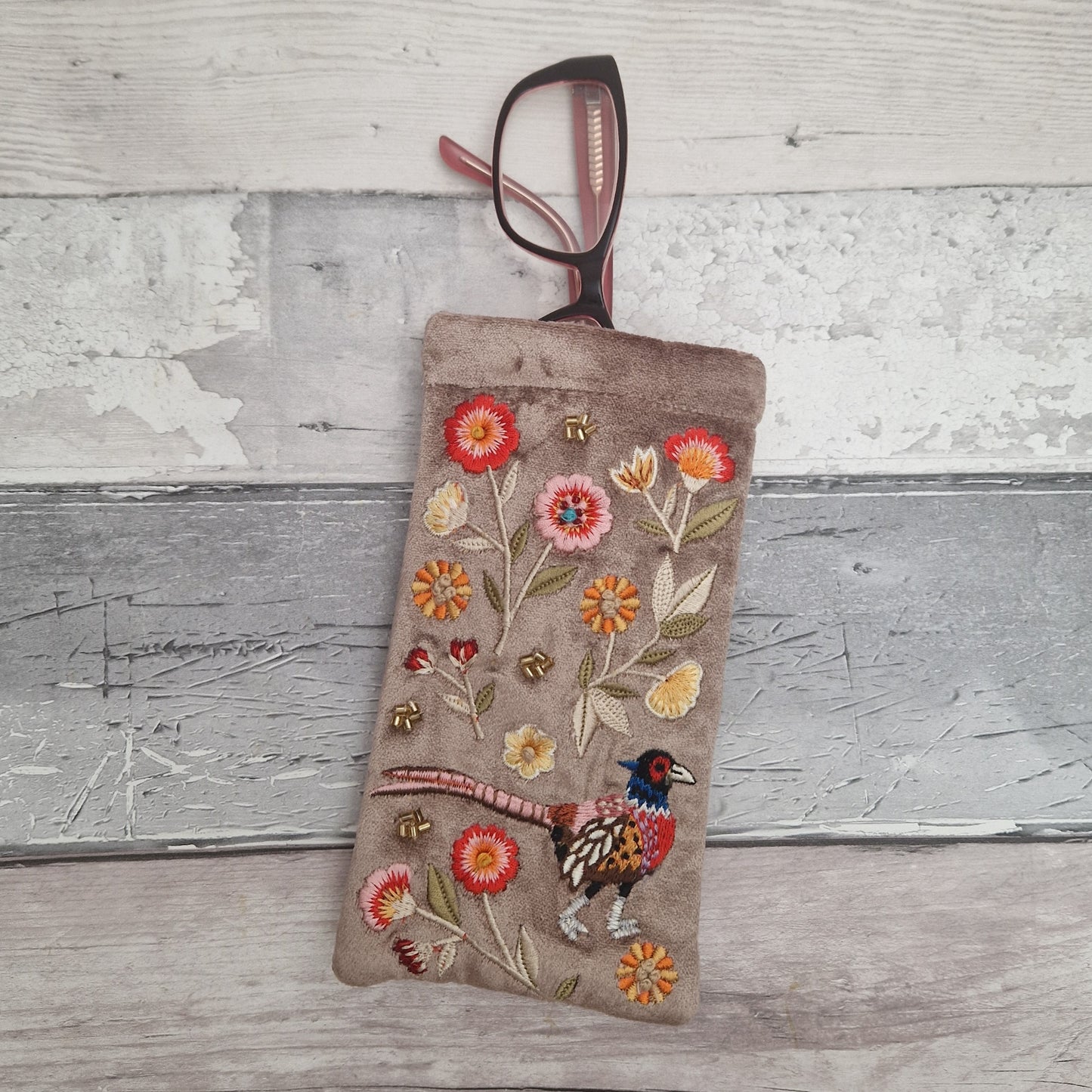Fawn coloured velvet glasses case decorated with an embroidered scene featuring a Pheasant in a flower garden. The scene is finished with beads and sequins.