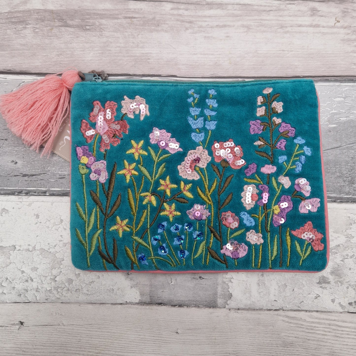 Turquoise velvet pouch decorated with embroidered flowers in pink and yellow. The pouch is finished in pink piping, a pink tassel and metallic sequins.