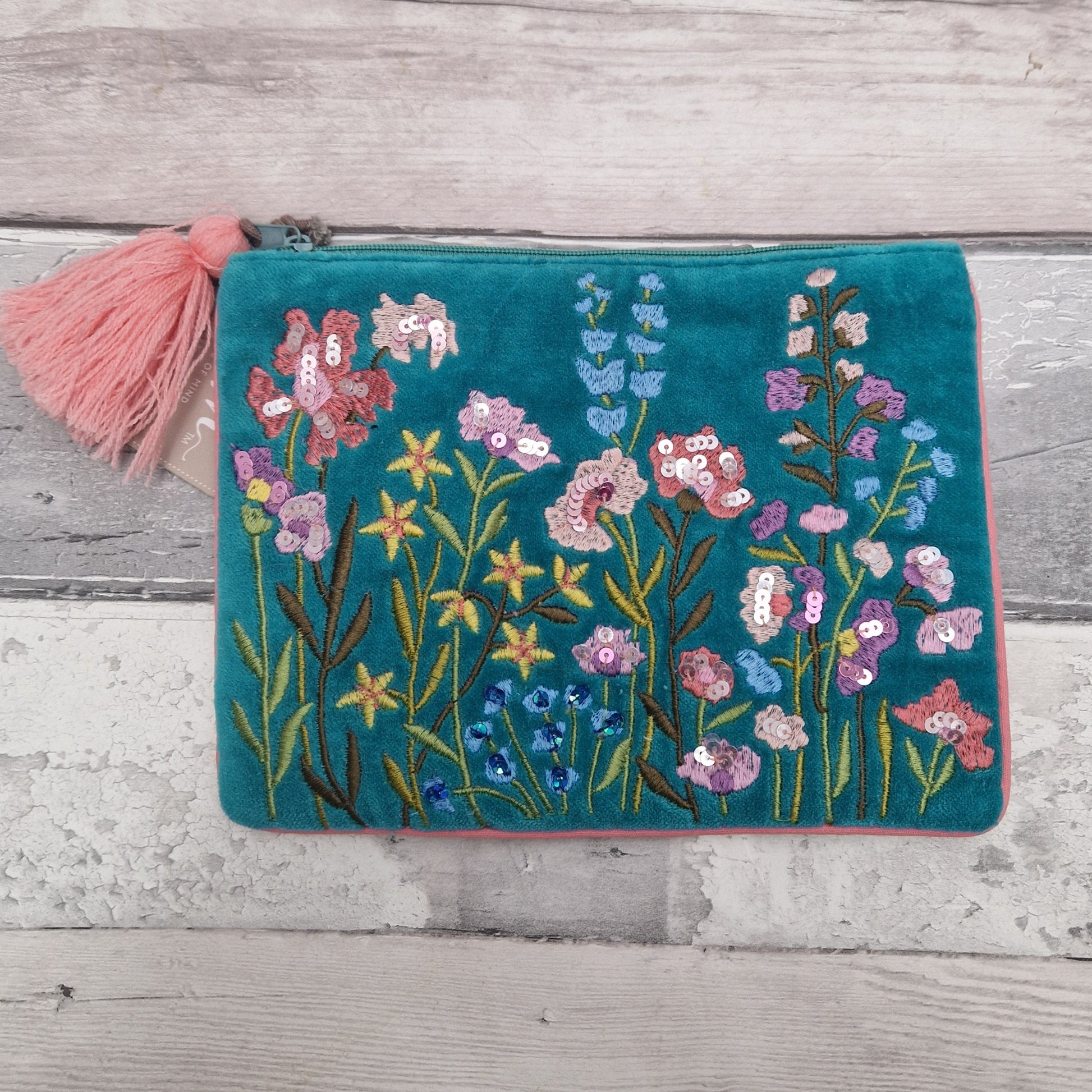 Turquoise velvet pouch decorated with embroidered flowers in pink and yellow. The pouch is finished in pink piping, a pink tassel and metallic sequins.