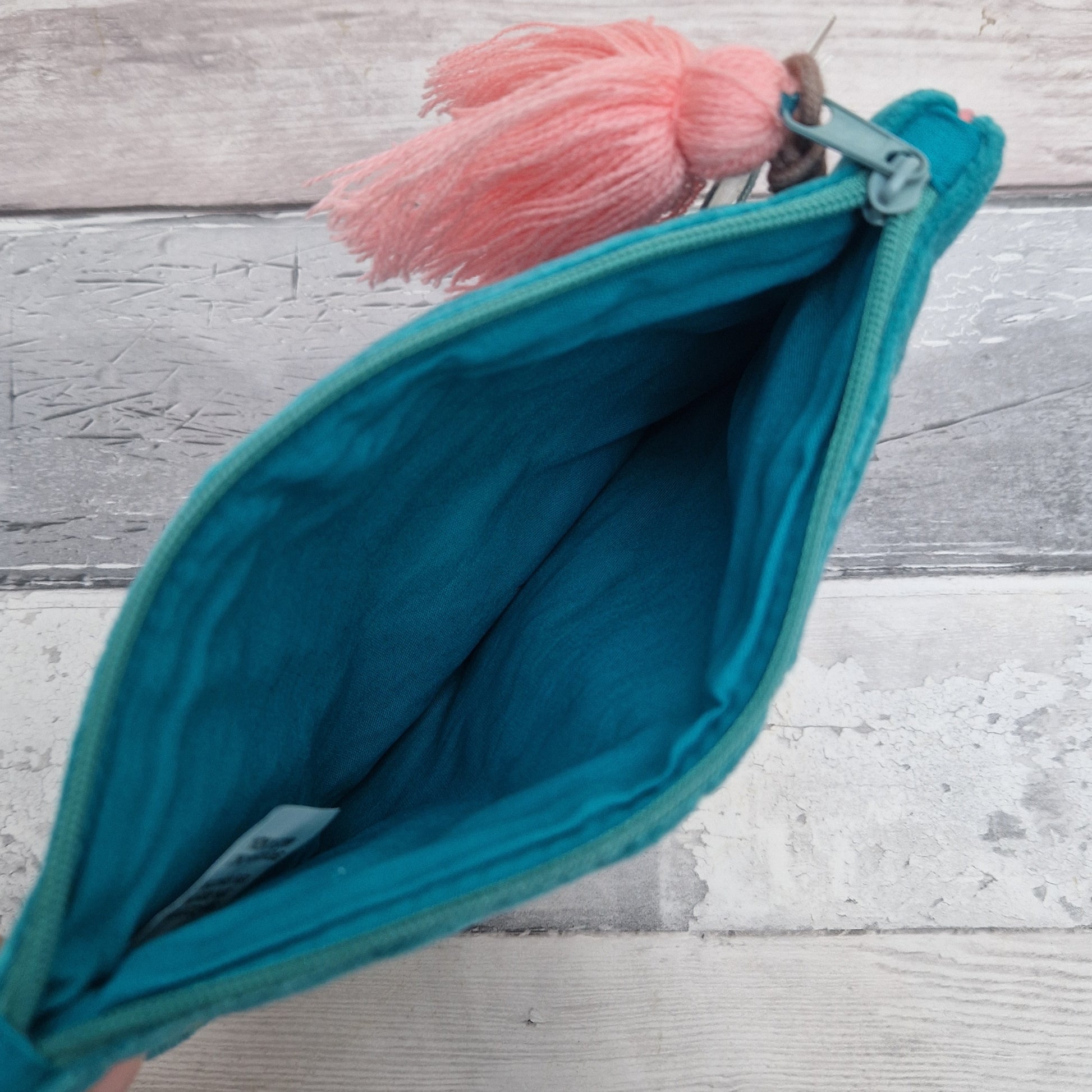 Turquoise pouch with pink tassel on a wooden surface