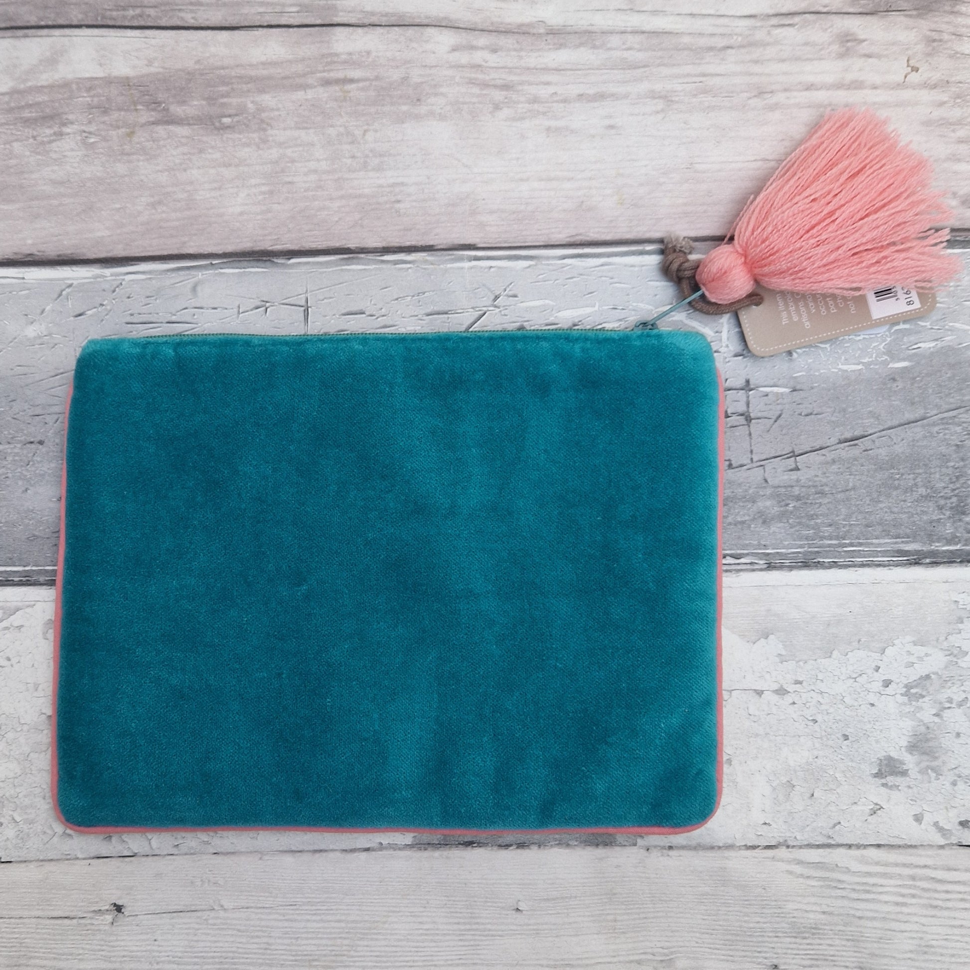 Turquoise teal cosmetic pouch with pink trim on a wooden surface