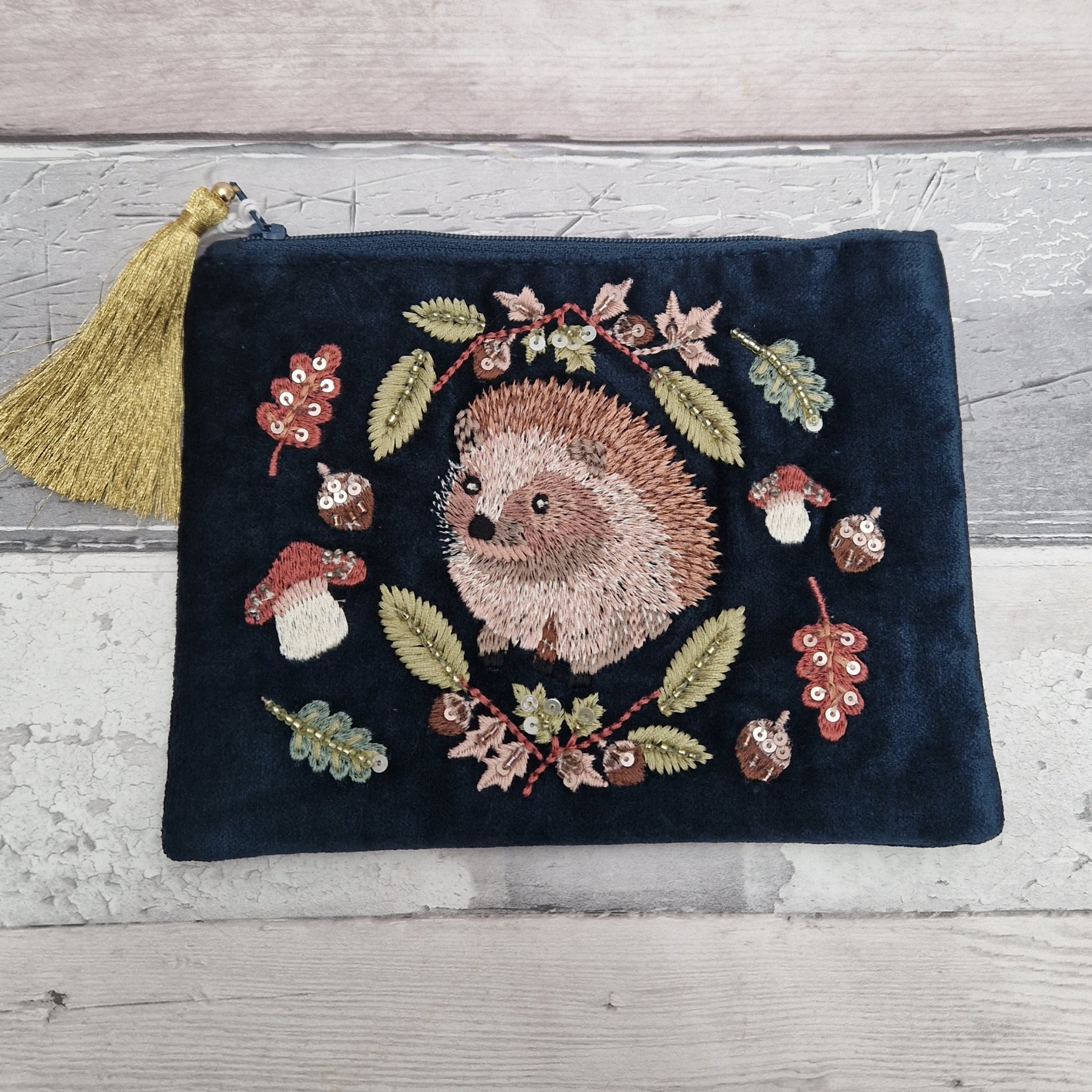 Navy velvet pouch with embroidered picture of a Hedgehog surrounded by woodland leaves, mushrooms and acorns. Zip closer with old tassel.
