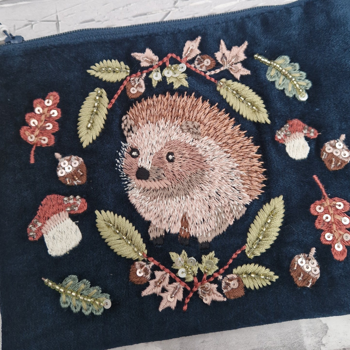 Navy velvet pouch with embroidered picture of a Hedgehog surrounded by woodland leaves, mushrooms and acorns. Zip closer with old tassel.