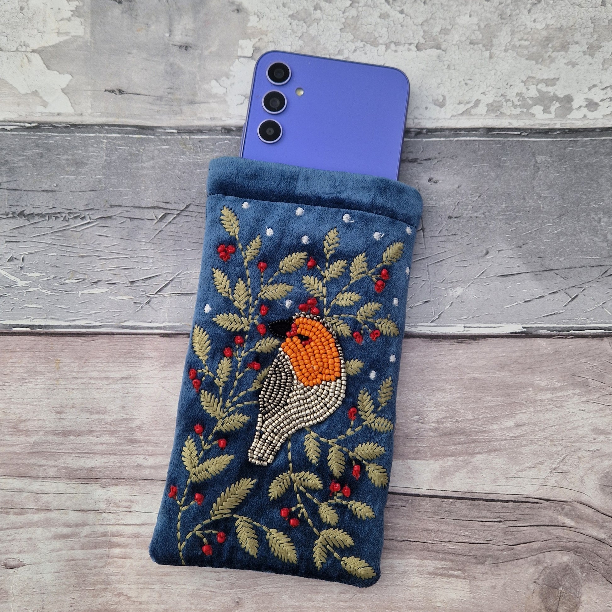 Embroidered phone case with a bird design on a wooden surface