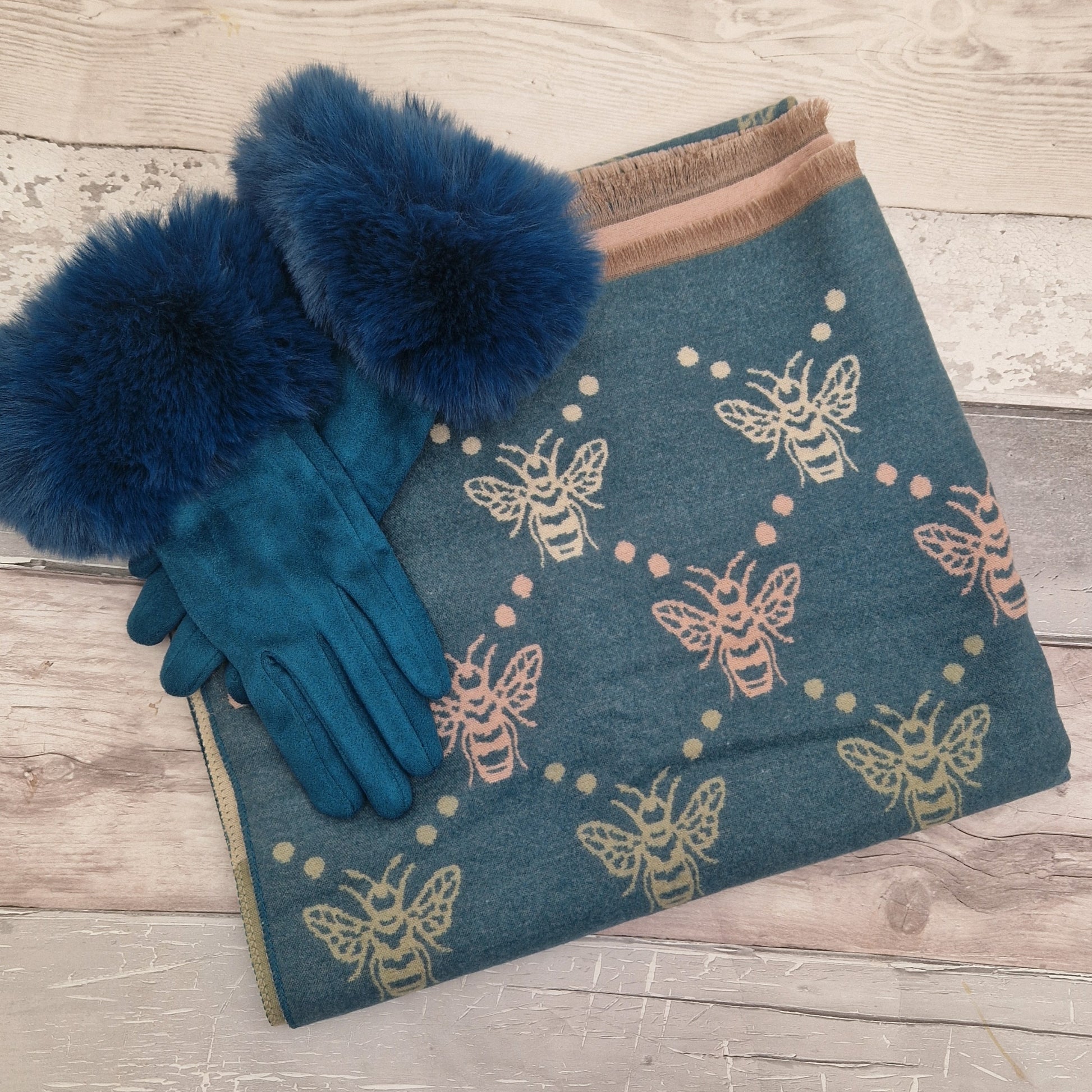 Blue gloves with fur cuffs and a blue scarf with bee pattern on a wooden surface