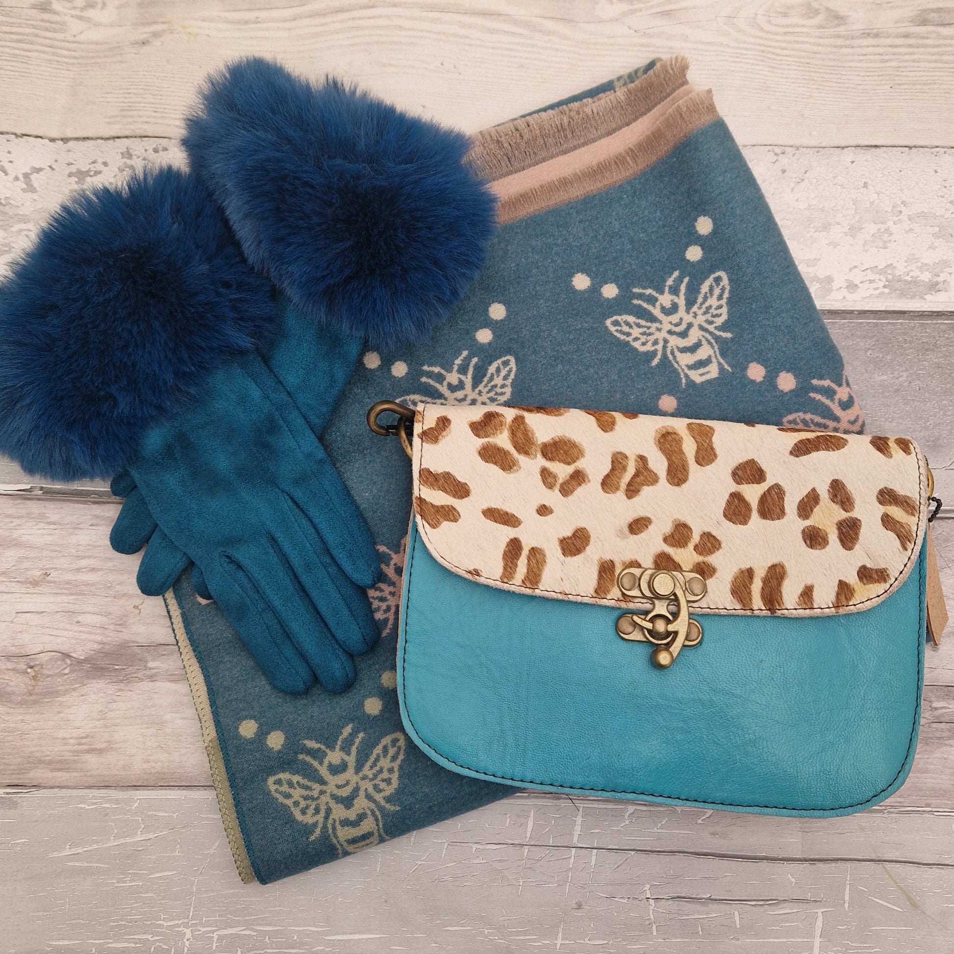 Blue gloves with fur cuffs, blue scarf with bee pattern, and blue handbag with animal print on a wooden surface.