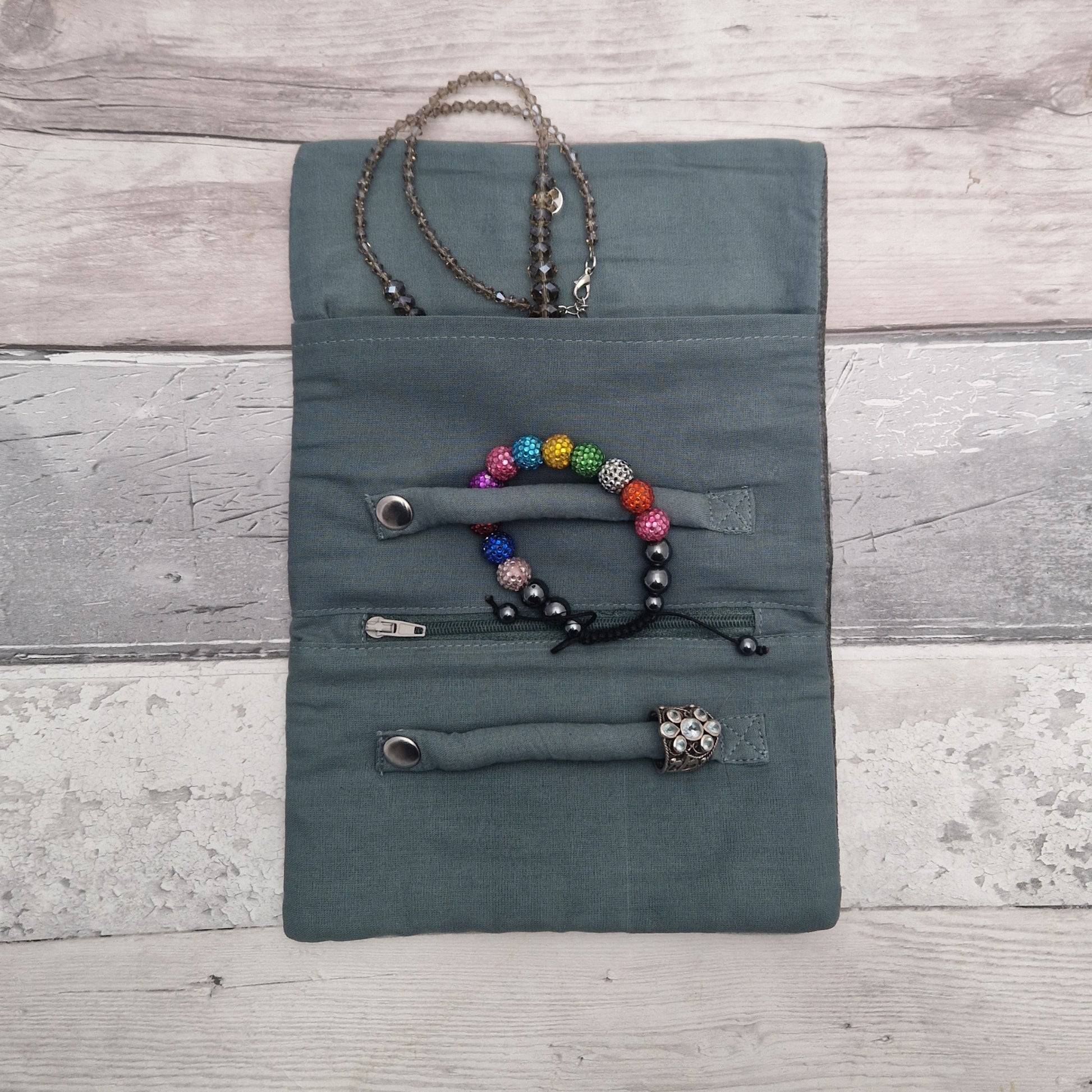 Gray jewelry pouch with necklaces and bracelets on a wooden surface