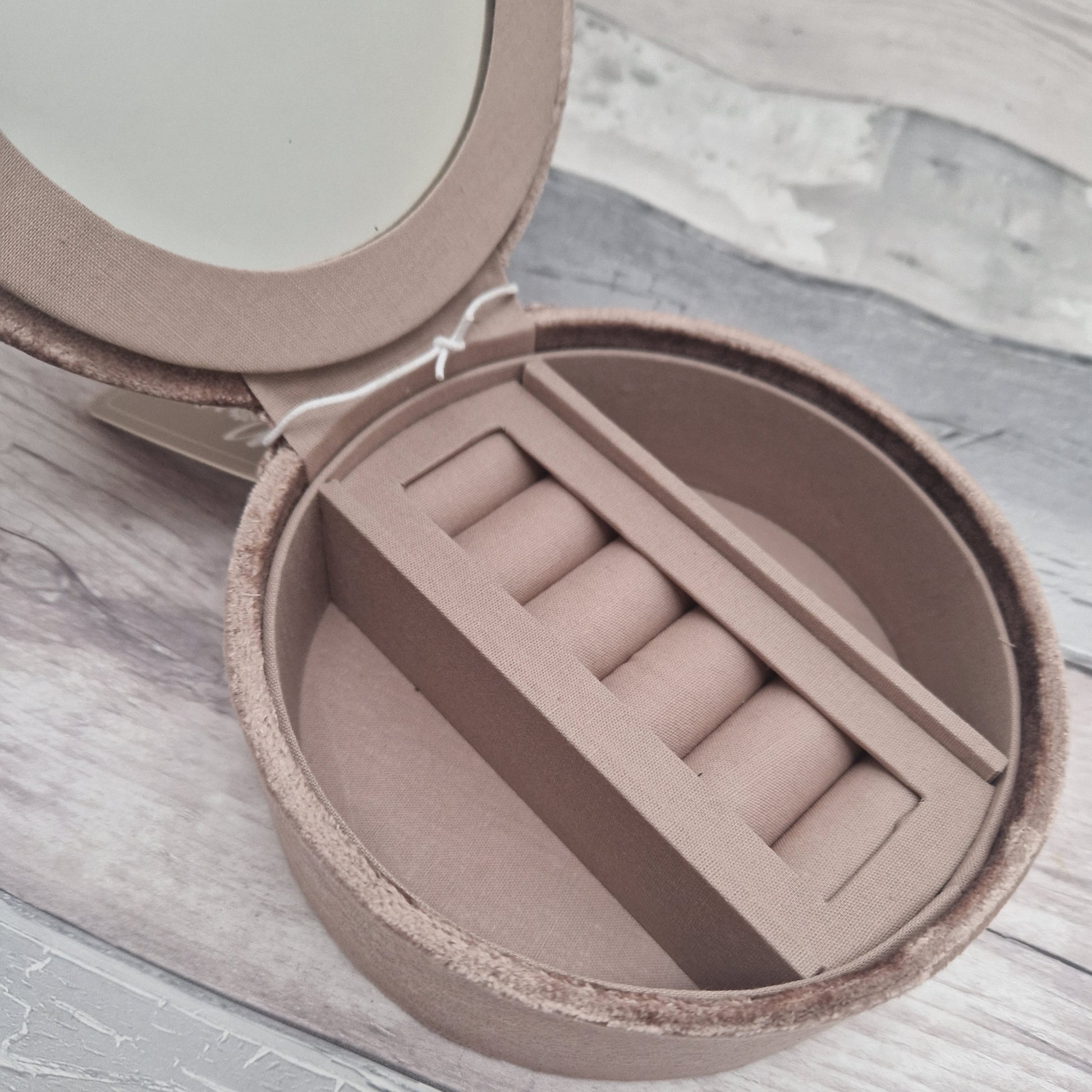 Round jewelry box with buff interior on a light wooden surface