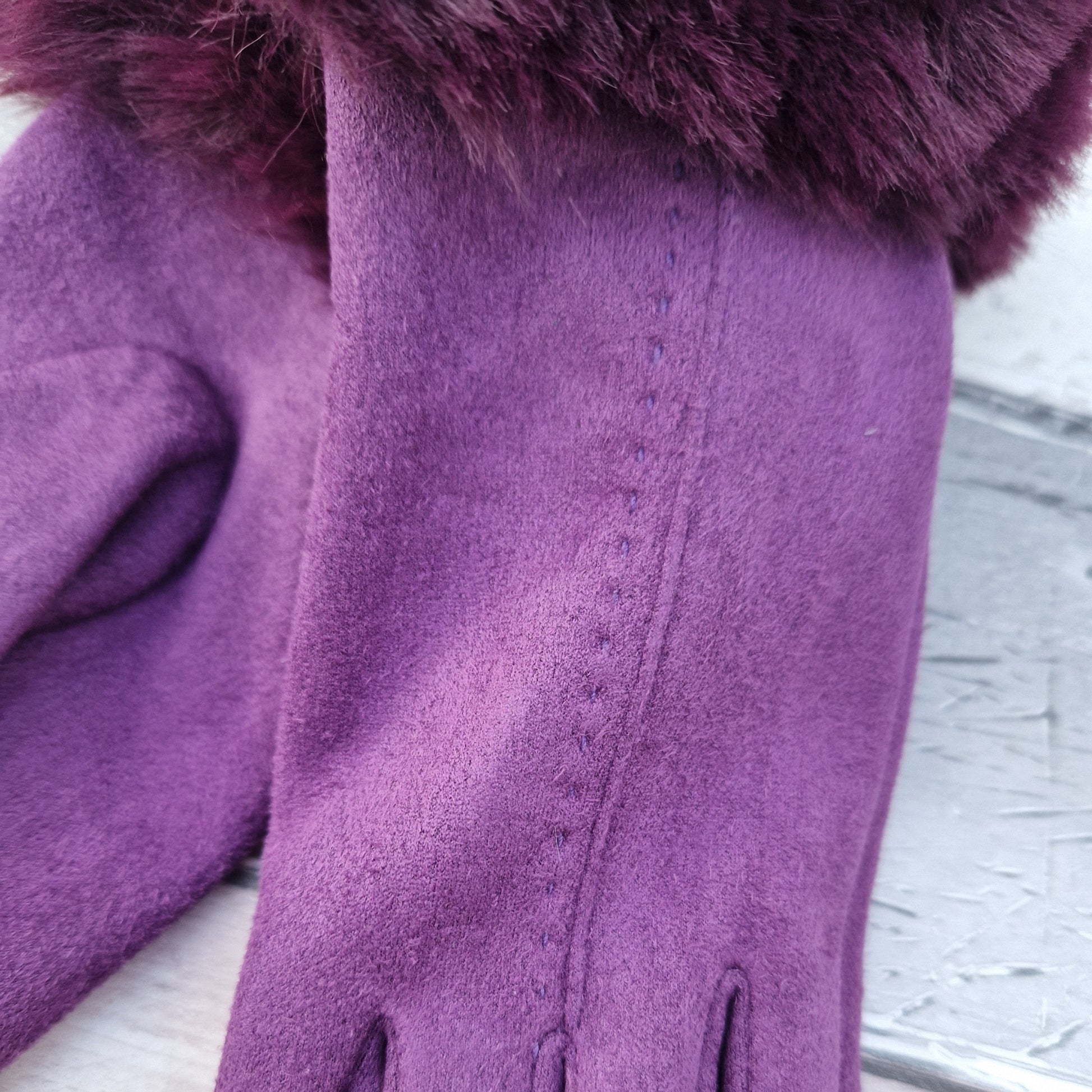 Purple coloured gloves with a faux fur trim and stitching detail down the back of the hand.