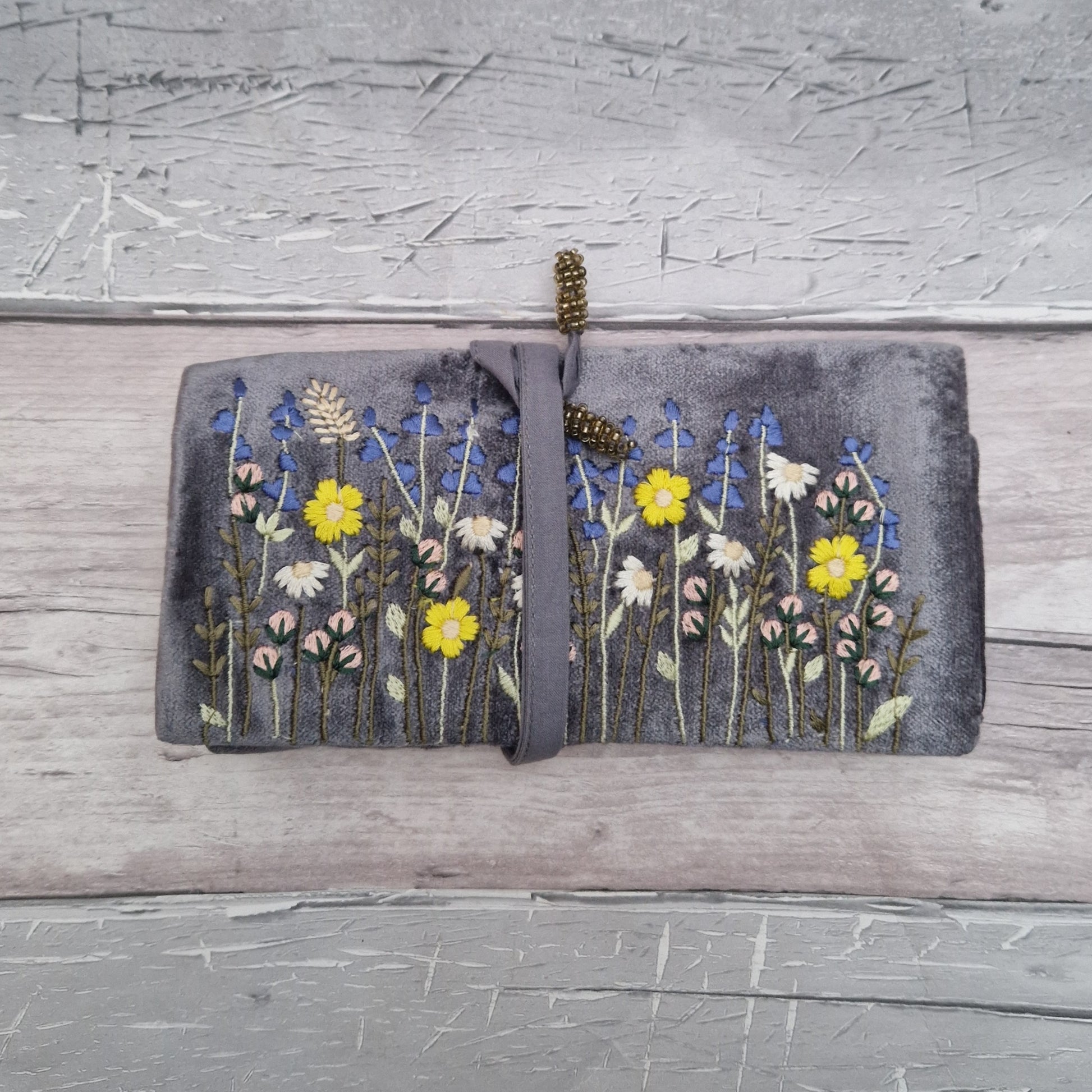 Silver grey velvet jewellery roll decorated with an embroidered freeze of wildflowers and lavender.