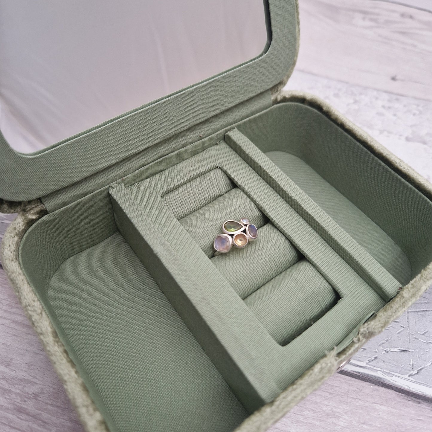 Green jewelry box with a ring inside on a light wooden surface