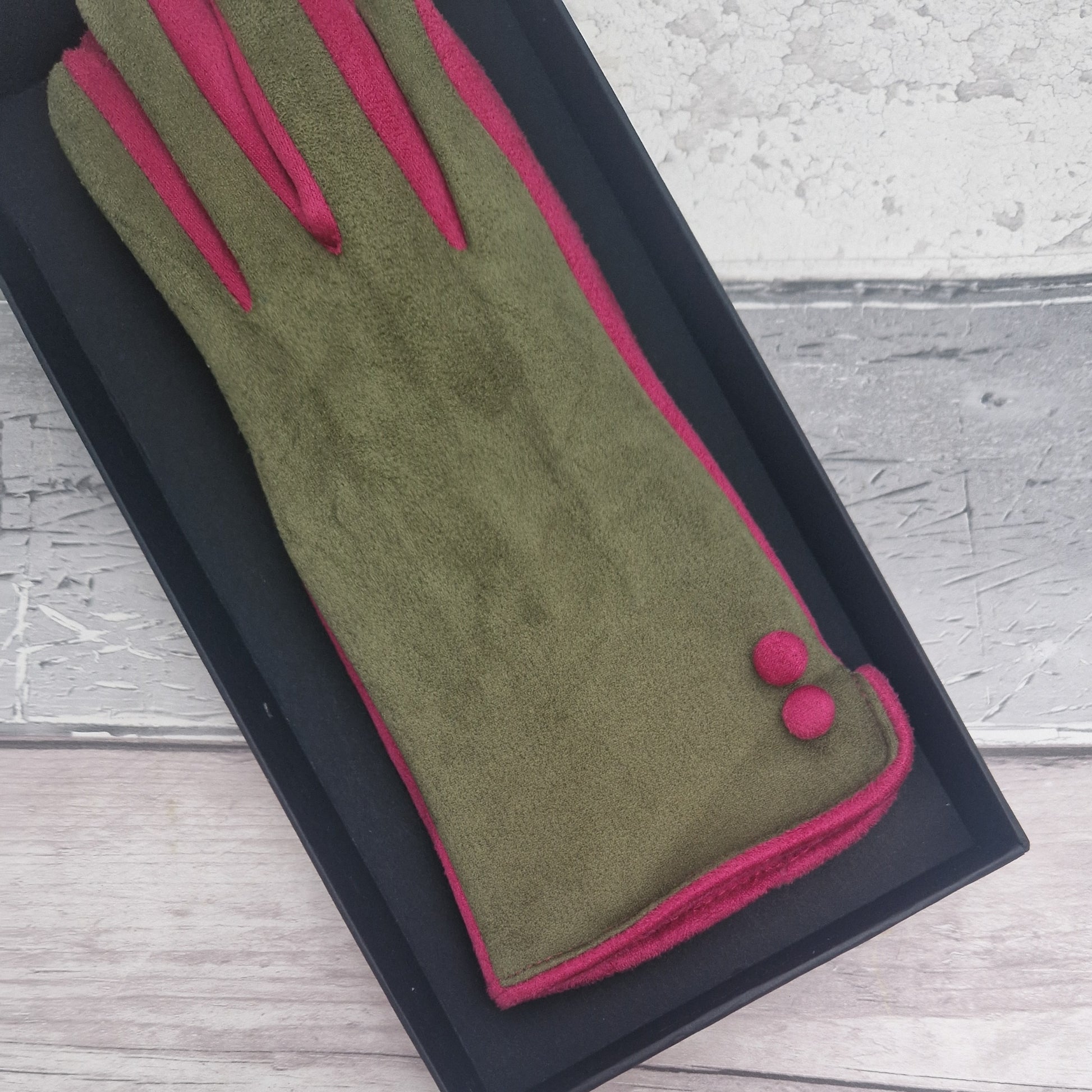 Olive green and hot pink coloured gloves with hot pink buttons presented in a black gift box.