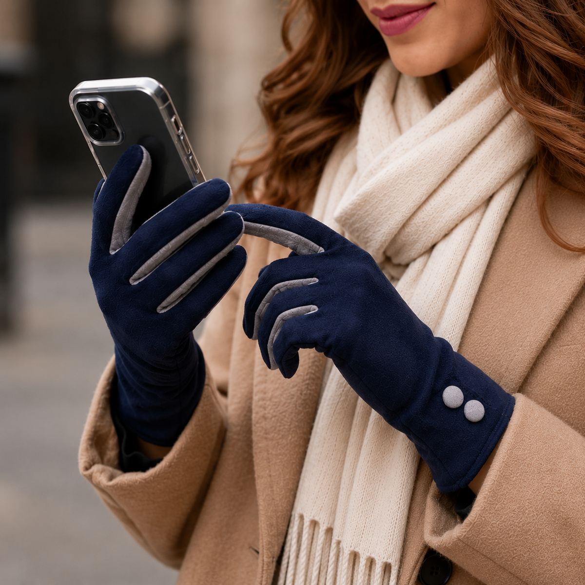 Person wearing navy gloves with grey accents, holding a phone, wearing a beige coat and scarf.