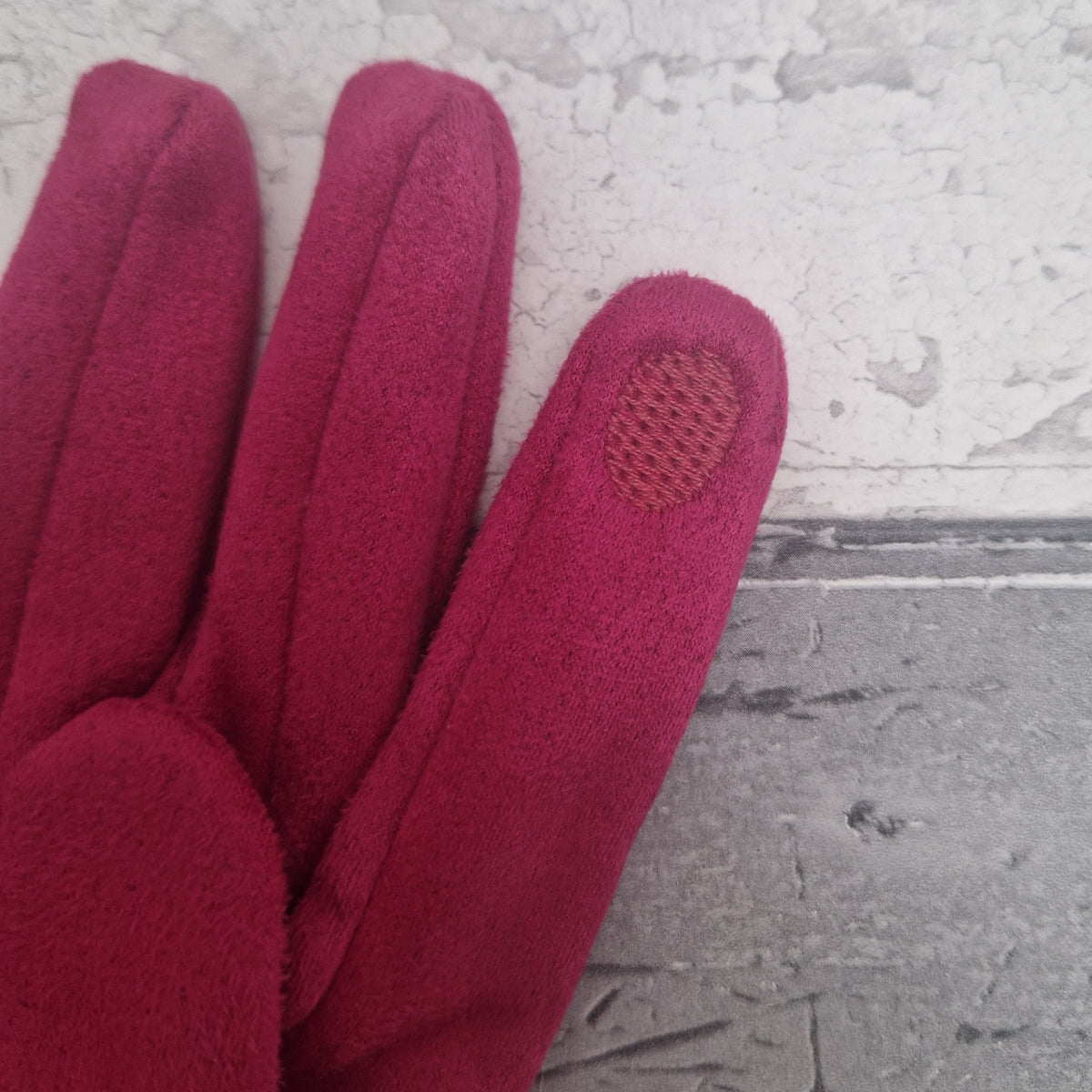 Hot Pink coloured glove with a textured touch screen tip on a gray surface