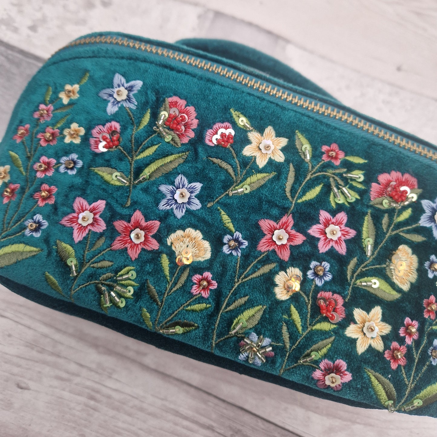 Close up view of a turquoise velvet vanity case decorated with embroidered flowers in primary colours.