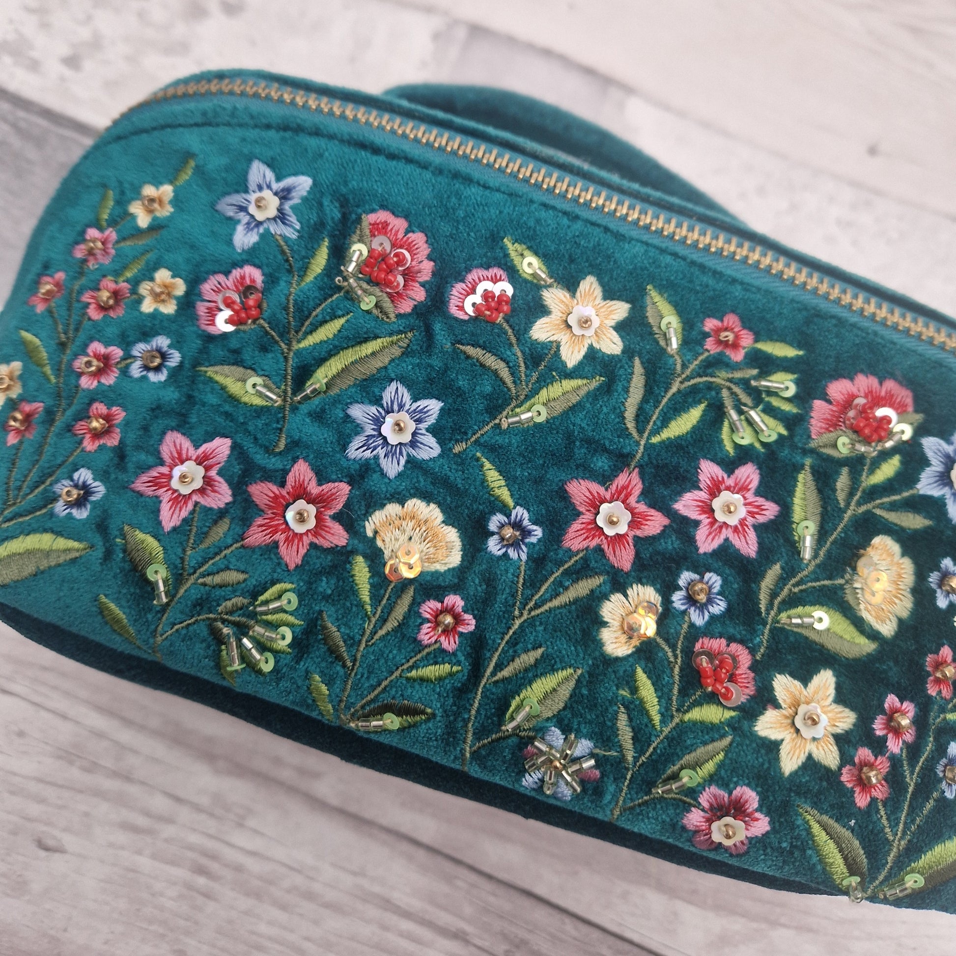 Close up view of a turquoise velvet vanity case decorated with embroidered flowers in primary colours.