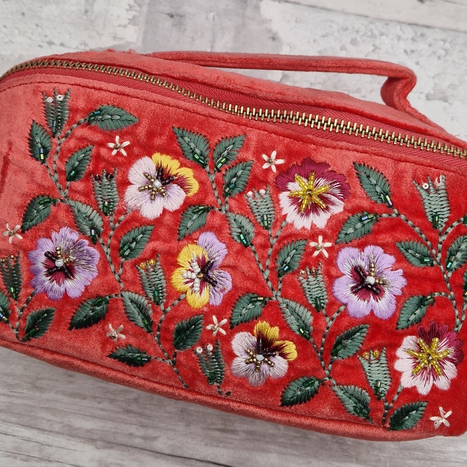 Close up view of embroidered panel on a salmon coloured velvet vanity case. Embroidery shows purple and yellow pansies finished with beads.