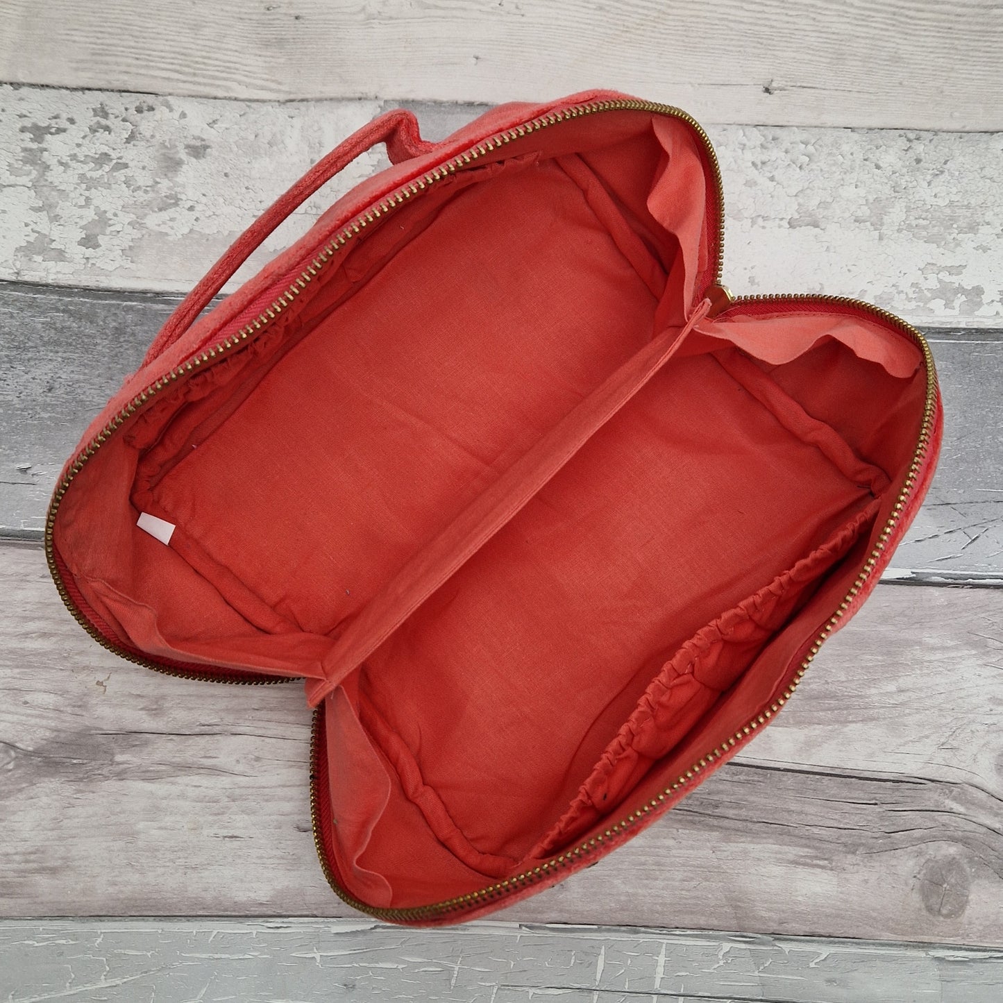 Inside view of a salmon coloured fold out vanity case showing central divider and elasticated pockets.