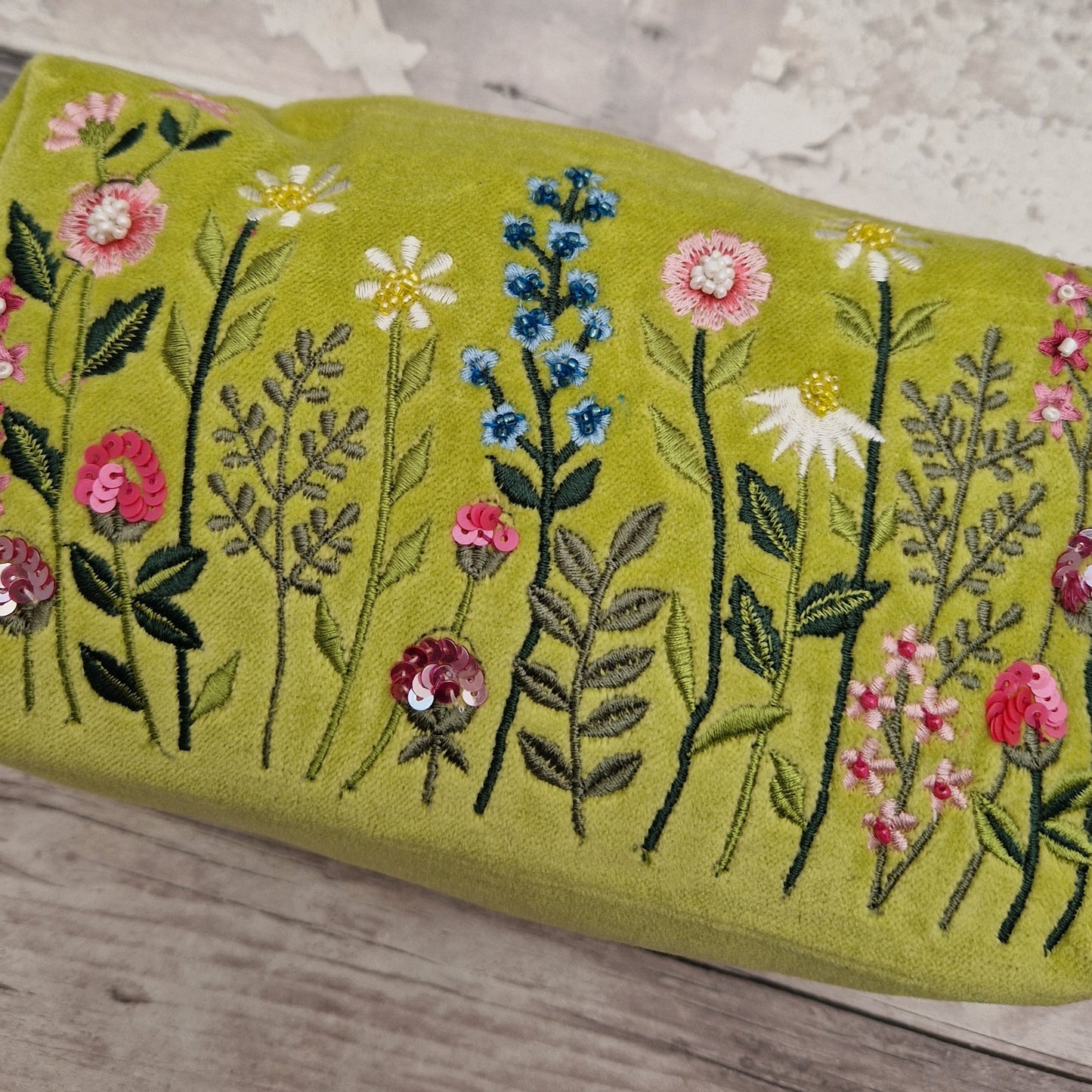 Close up photo of a Lime green velvet toiletry bag decorated with embroidered flowers, finished with sequins and beads.