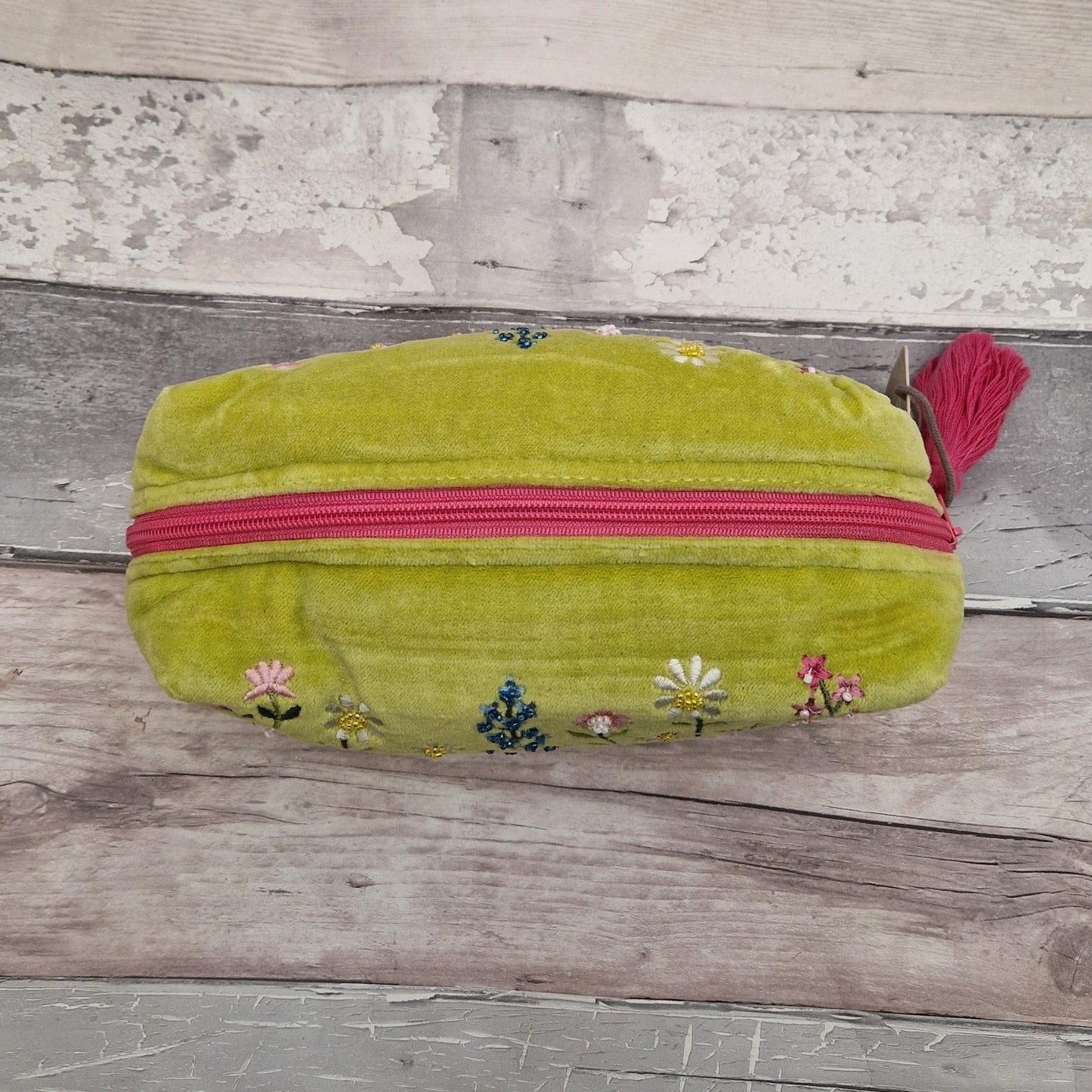 Top down view of a lime green velvet toiletry bag with a contrasting pink zip and tassel pull.