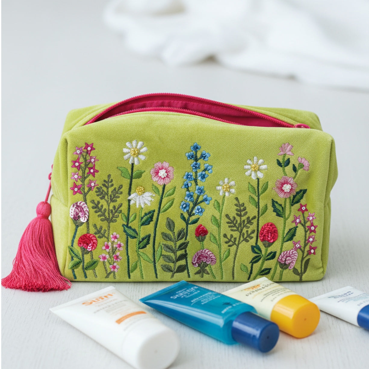 Lime green velvet toiletry bag decorated with embroidered flowers, finished with sequins and beads in a bathroom scene with  selection of sun tan lotion bottles in foreground.