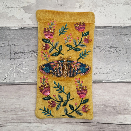 Mustard coloured velvet glasses case with a stylised image of a tiger moth embroidered with pink and blue flowers.