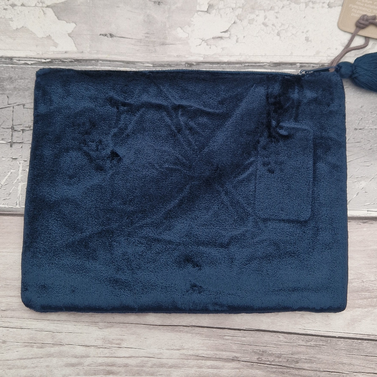 A dark navy blue plush velvet pouch or clutch with a zipper closure, resting on a light-colored rustic wooden surface.