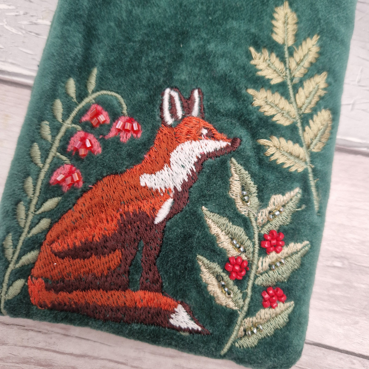 Close up view of a green velvet glasses case decorated with an embroidered fox sat elegantly amongst woodland ferns.