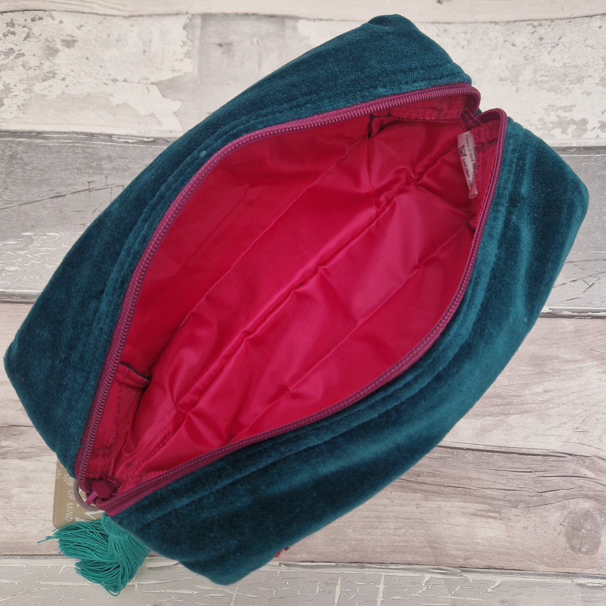 Inside view of a teal blue velvet wash bag revealing a hot pink waterproof interior lining.